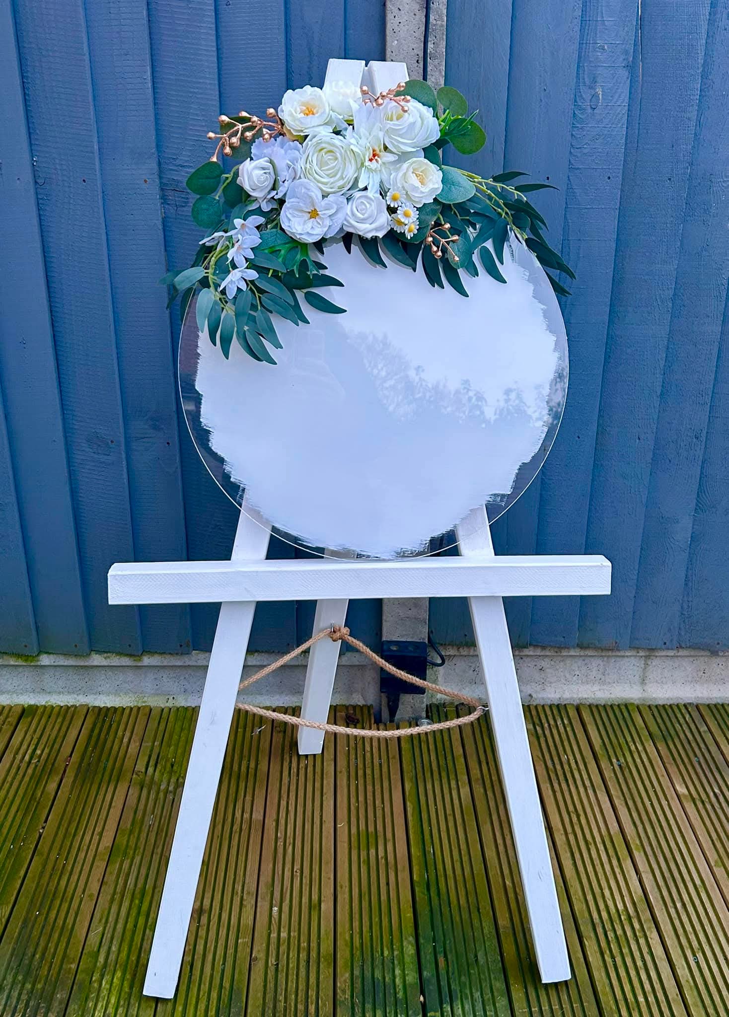 Round acrylic sign with a white floral and eucalyptus arrangement on a white easel