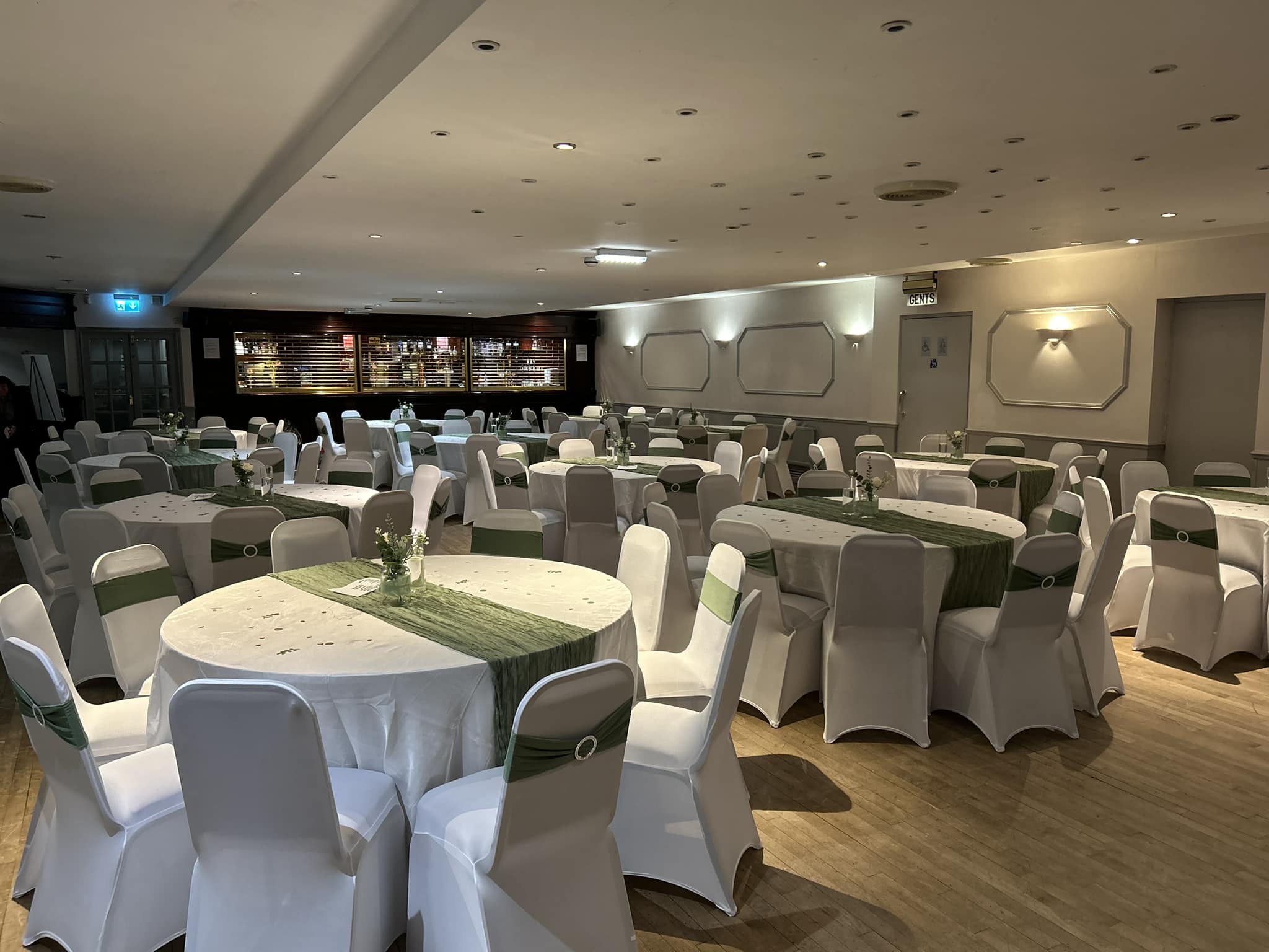 Banqueting room styled with white chair covers and sage green sashes and runners